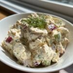 Close-up of creamy greek yogurt chicken salad mixed with red onion and celery, topped with fresh dill.