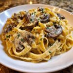 Close-up of creamy mushroom pasta featuring fettuccine noodles coated in a rich sauce and topped with sautéed mushrooms and parsley.