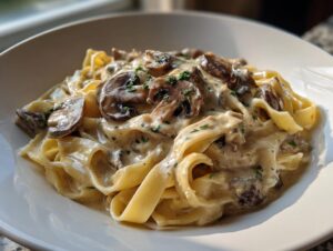 A close-up of creamy mushroom pasta featuring fettuccine noodles coated in a rich white sauce and topped with sliced mushrooms.