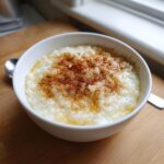 A close-up of creamy rice pudding in a white bowl, topped generously with ground cinnamon.