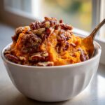 A close-up of a white bowl filled with creamy crockpot sweet potato casserole topped generously with candied pecans.