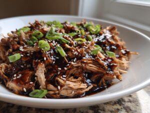 Shredded crockpot teriyaki chicken coated in rich sauce, topped with sesame seeds and sliced green onions.