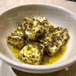 Close-up of cubes of marinated cheese soaking in olive oil and covered with dried herbs and spices.