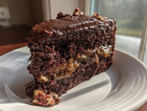 A rich slice of german chocolate cake with gooey filling and chocolate frosting, sitting on a white plate.