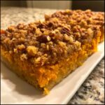 Close-up of a slice of easy sweet potato casserole featuring a bright orange filling and a crunchy pecan streusel topping.