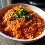 Close-up of a white bowl filled with bright orange, fluffy spanish rice, topped with fresh cilantro.