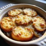 Close-up of a baked french onion soup recipe in a crock, topped with melted, bubbly cheese on toasted bread slices.