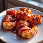 Close-up of several perfectly cooked bacon wrapped shrimp glazed with a sweet and savory sauce, served on a white plate.