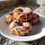 A stack of four golden brown baked apple fritters heavily drizzled with white glaze, sitting on a white plate.