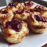 Close-up of golden baked brie bites made with puff pastry and topped with dark red jam.