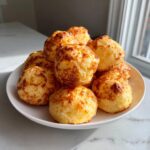 A pile of freshly baked, golden brown brazilian cheese bread puffs stacked high on a white plate.