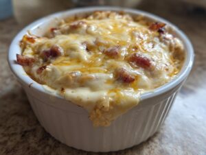 Close-up of a bubbling, cheesy reuben dip baked in a white ramekin, showing melted cheese and bits of corned beef.