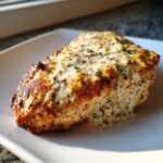 Close-up of a perfectly cooked baked ranch chicken breast topped with creamy ranch sauce and herbs.