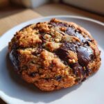 A thick, chunky levain bakery chocolate chip cookie loaded with melted chocolate pools and nuts, sitting on a white plate.