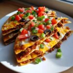 Four stacked slices of homemade Mexican pizza topped with melted cheese, seasoned ground beef, diced tomatoes, onions, and black olives.