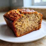 Close-up of a thick slice of moist best banana bread showing the speckled interior and caramelized top, served on a white plate.