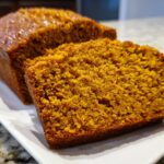 Close-up of two thick slices of moist pumpkin bread showing its rich orange color and texture.