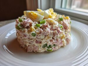 A molded serving of creamy ham salad recipe mixed with green onions and topped with sliced hard-boiled egg.