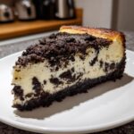 A close-up of a rich slice of baked Oreo cheesecake with a dark cookie crust and crumb topping.