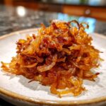 A close-up of a mound of deeply golden brown caramelized onions on a light-colored plate.