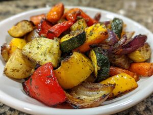 Close-up of colorful, perfectly roasted vegetables including potatoes, carrots, zucchini, peppers, and onions seasoned with herbs.