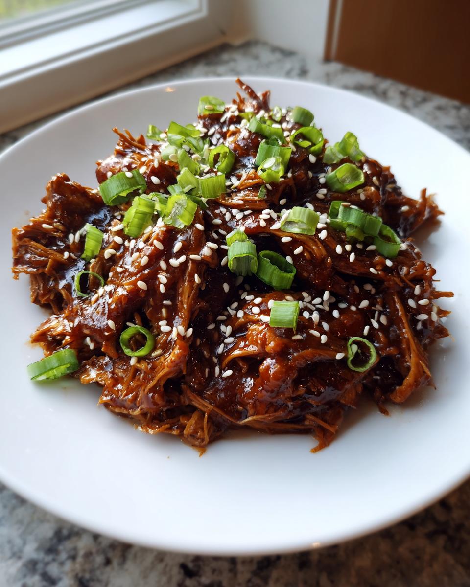 A serving of saucy, shredded crockpot teriyaki chicken topped with sesame seeds and sliced green onions.