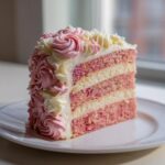 A tall slice of raspberry rose cake showing alternating pink and white layers with exterior frosting piped into pink and white rosettes.