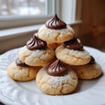 A stack of soft, sugar-coated kiss cookies topped with a dollop of rich chocolate frosting.