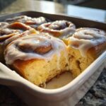 Close-up of fluffy sourdough discard cinnamon rolls topped with white icing in a white baking dish.