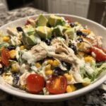 Close-up of a delicious southwest chicken salad topped with avocado, corn, black beans, and creamy dressing.