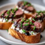 Close-up of perfectly cooked steak crostini bites topped with creamy cheese, balsamic glaze, and fresh chives.