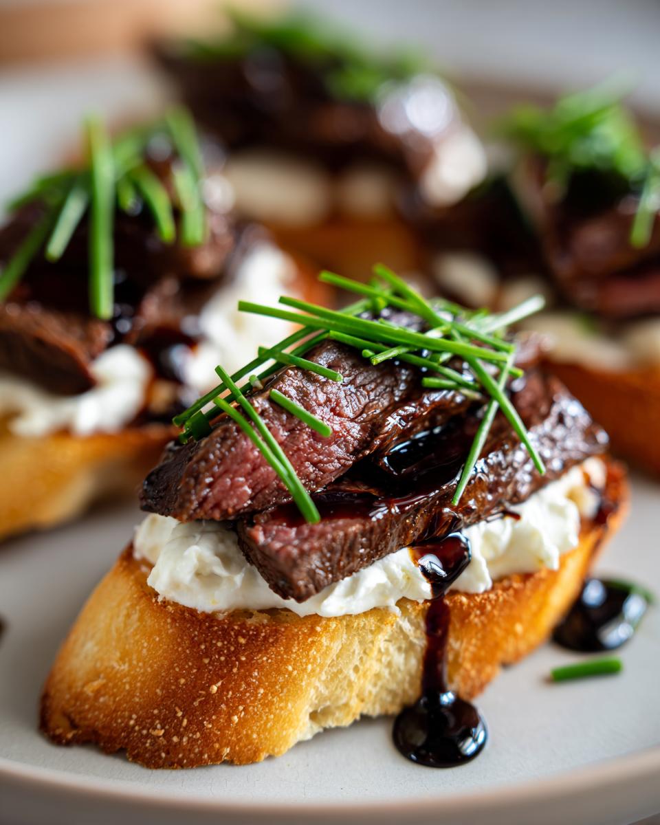 Close-up of a perfectly cooked steak crostini topped with creamy cheese and fresh chives.