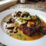 A perfectly cooked steak generously covered in a creamy, savory mushroom sauce and fresh parsley.