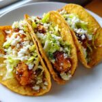 Three crispy, golden-fried potato tacos filled with seasoned potato chunks, shredded lettuce, and crumbled white cheese.