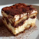 Close-up of a decadent slice of tiramisu cheesecake layered with cream and coffee-soaked ladyfingers, dusted with cocoa.