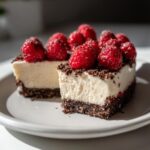 Two slices of white chocolate mousse tart with a dark chocolate crust, topped with fresh raspberries.