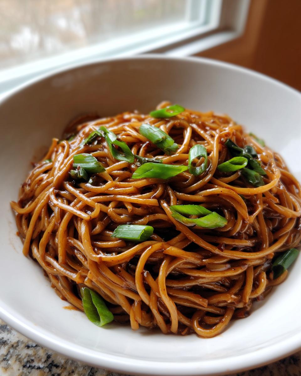 A close-up of glossy, dark brown garlic noodles topped with bright green sliced scallions in a white bowl.