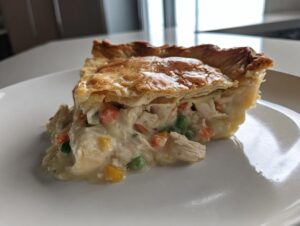 A close-up of a slice of amazing chicken pot pie recipe showing flaky crust and creamy filling with chicken, peas, and carrots.
