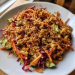 A bowl of amazing crispy rice salad topped with shredded carrots, cucumber, red cabbage, and peanut sauce.