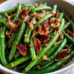 Close-up of vibrant green beans tossed with crispy bacon bits and caramelized onions.