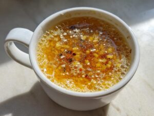 Close-up of hot pastina soup with small pasta grains floating in a rich yellow broth, seasoned with spices, served in a white mug.