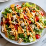 Close-up of a vibrant southwest salad featuring grilled chicken, black beans, tomatoes, and tortilla chips drizzled with orange dressing.
