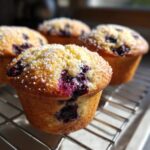 Close-up of golden blueberry cottage cheese muffins topped with coarse sugar, cooling on a wire rack.