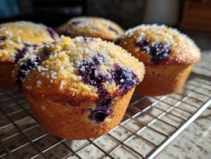 Close-up of golden blueberry cottage cheese muffins cooling on a wire rack, topped with coarse sugar.