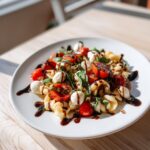 A vibrant serving of caprese pasta salad featuring pasta shells, mozzarella balls, tomatoes, and basil drizzled with balsamic.