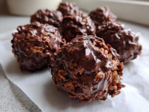 Close-up of several glossy chocolate rice krispie balls resting on white parchment paper.