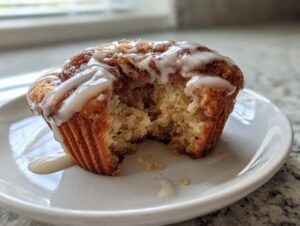 Close-up of a delicious cinnamon roll muffin with a bite taken out, drizzled with white icing.