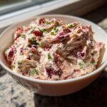 Close-up of creamy cranberry jalapeno cream cheese dip topped with chives in a white bowl.
