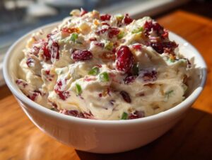 A close-up shot of a white bowl filled with creamy cranberry jalapeno cream cheese dip, featuring red cranberries and green peppers.