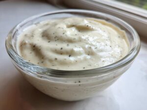 Close-up of thick, creamy white chia seed pudding speckled with dark vanilla bean or spice specks in a small glass bowl.